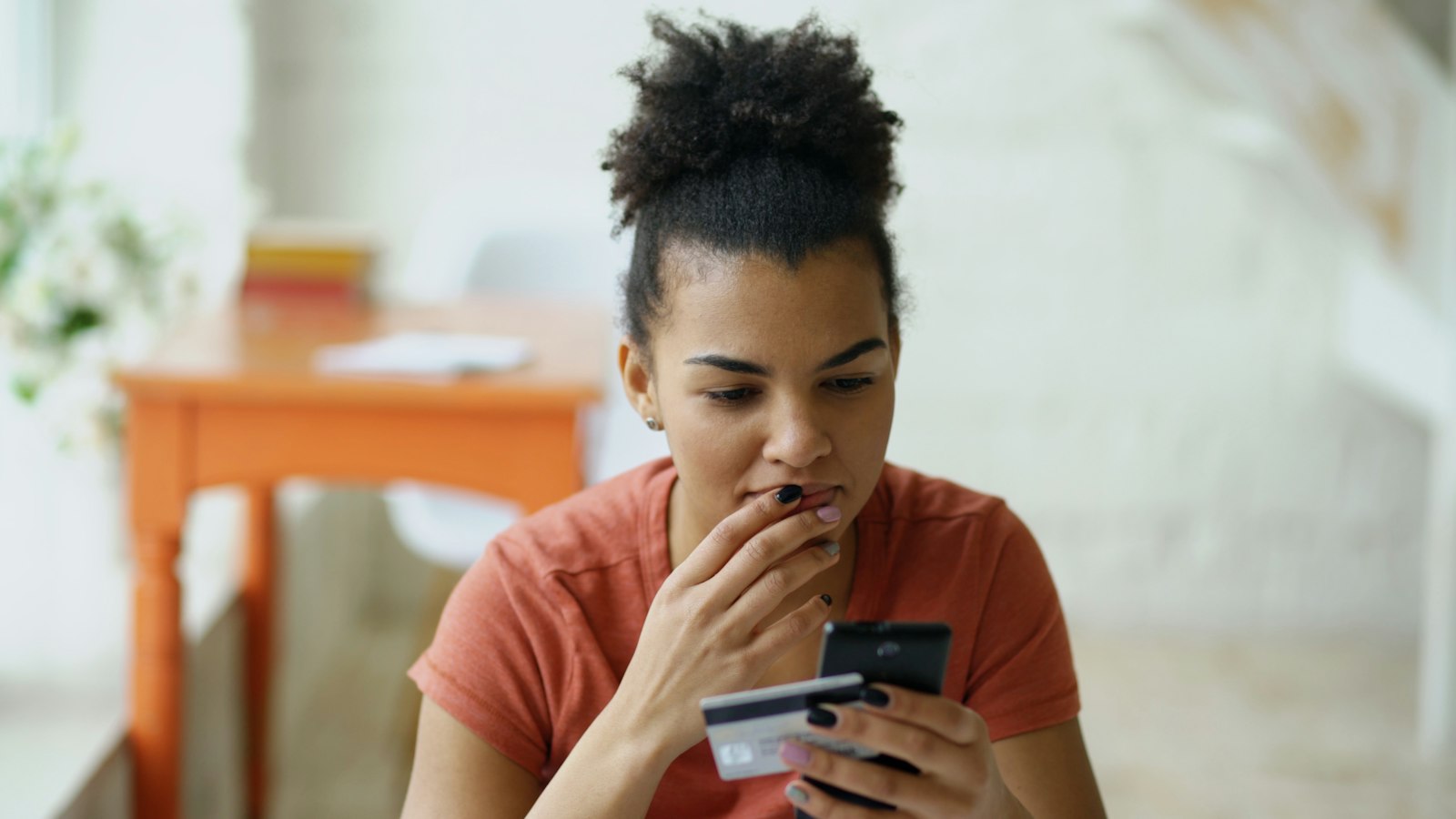 A woman checks her phone while holding a bank card