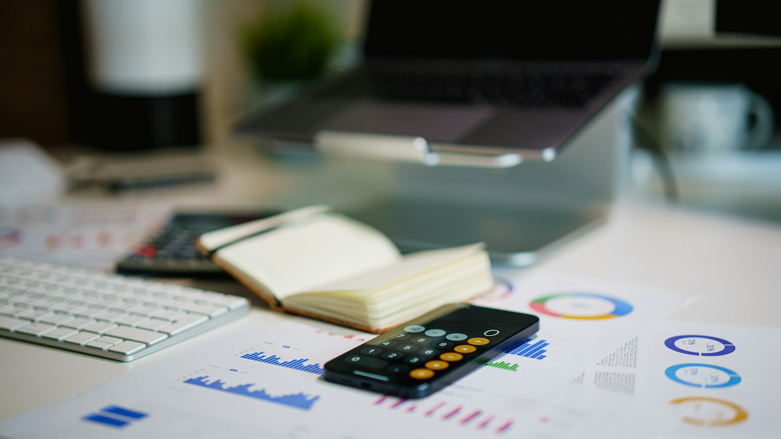 A calculator phone rests on financial documents beside a notebook
