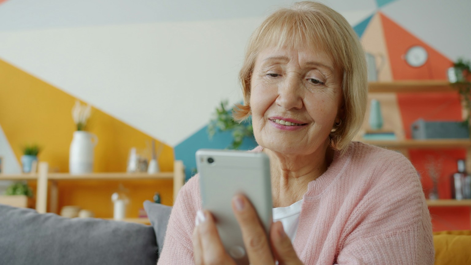 An older woman looks at a smartphone while sitting at home