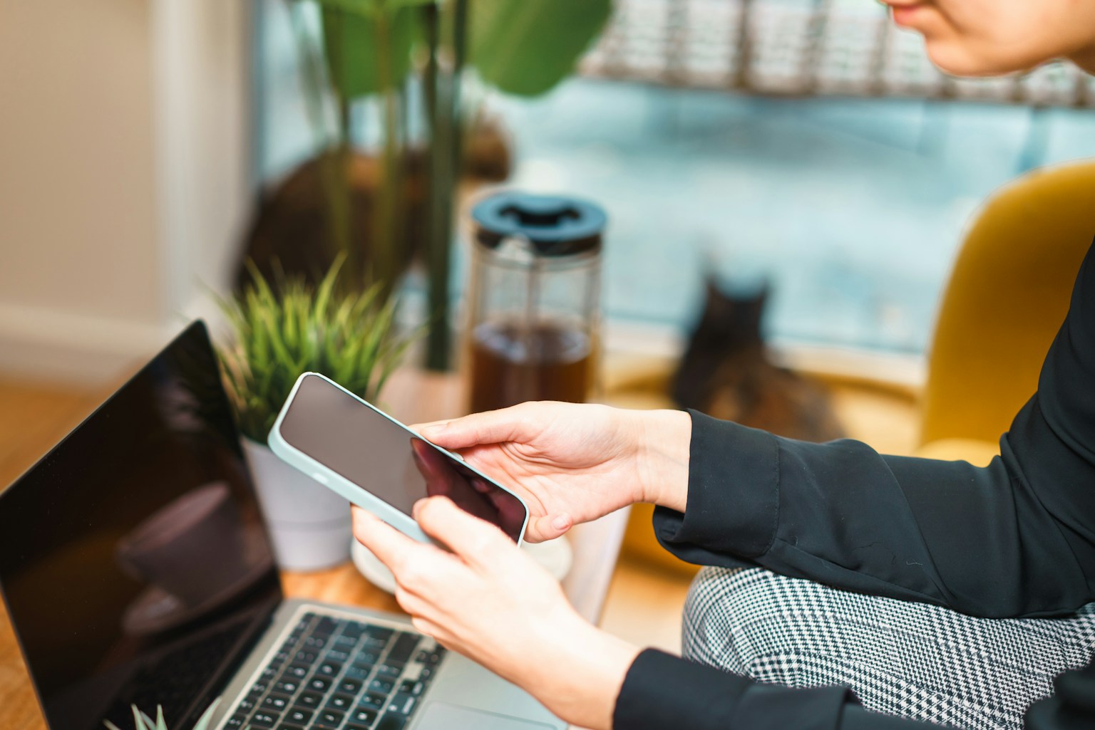 A person uses a smartphone while working at a laptop